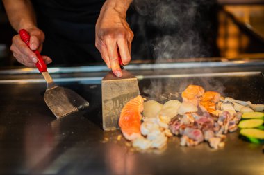 Şefin elleri teppanyaki yerine spatula ile. Sebze pişirmek et ve deniz ürünleri sıcak hibachi ızgara masasında. Geleneksel Japon mutfağı. Teppan gösterisi