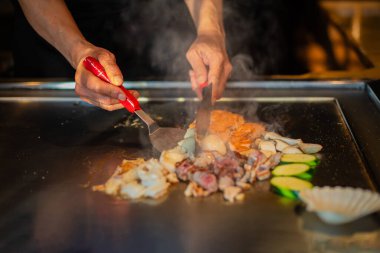 Şefin elleri teppanyaki yerine spatula ile. Sebze pişirmek et ve deniz ürünleri sıcak hibachi ızgara masasında. Geleneksel Japon mutfağı. Teppan gösterisi