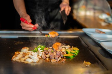 Şefin elleri teppanyaki yerine spatula ile. Sebze pişirmek et ve deniz ürünleri sıcak hibachi ızgara masasında. Geleneksel Japon mutfağı. Teppan gösterisi