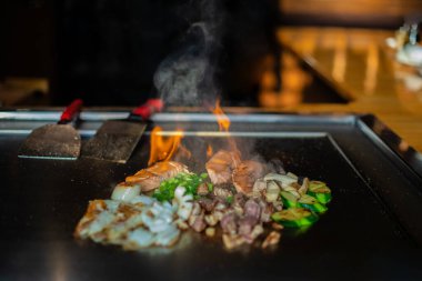 Şefin elleri teppanyaki yerine spatula ile. Sebze pişirmek et ve deniz ürünleri sıcak hibachi ızgara masasında. Geleneksel Japon mutfağı. Alevli Teppan gösterisi