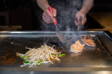Şefin elleri teppanyaki yerine spatula ile. Sebze pişirmek et ve deniz ürünleri sıcak hibachi ızgara masasında. Geleneksel Japon mutfağı. Teppan gösterisi
