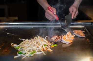 Şefin elleri teppanyaki yerine spatula ile. Sebze pişirmek et ve deniz ürünleri sıcak hibachi ızgara masasında. Geleneksel Japon mutfağı. Teppan gösterisi
