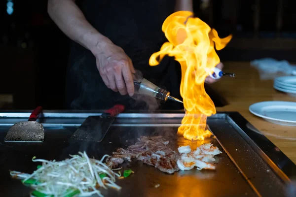 シェフの手は ティッパニャキの上に スパトゥーラで ホットハイチグリルテーブルで野菜肉や魚介類を調理する 日本の伝統料理 テッパンショー — ストック写真