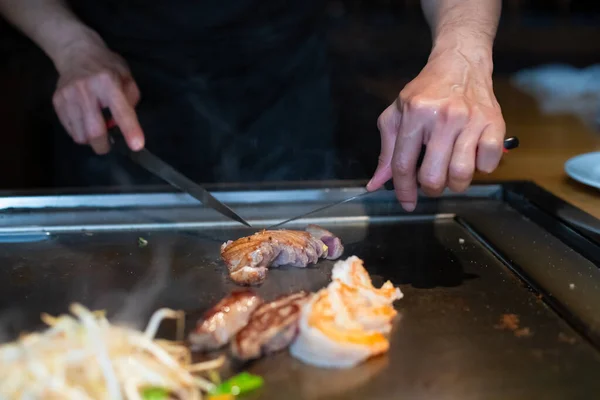 主厨的手 用平底锅盖着平底锅 将蔬菜 肉和海鲜放在火热的平八烤桌上烹调 传统的日本菜 Teppan秀 免版税图库图片