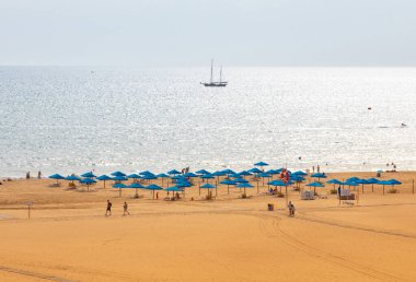 Portimao, Portiman, Algarve, Portekiz. 27.09.20.sıra iskemle ve mavi şemsiyeler kumlu sarı plajda. Avrupa seyahati ve tatil konsepti