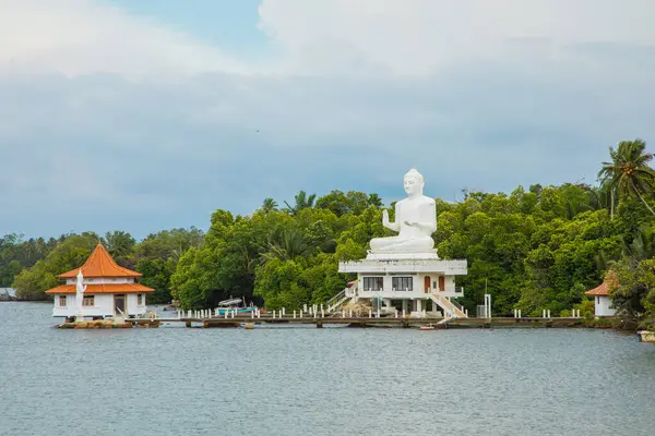 Beruwala,Sri Lanka. 02 Şubat 2023. Beyaz Buda figürü gölün üzerinde oturuyor. Arka plan güzel doğa ağaçları, mavi gökyüzü. Asya seyahati ve din kavramı