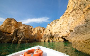 Güzel kayalıkların ve kemerlerin arka planında turuncu can simidi olan beyaz bir tekne.
