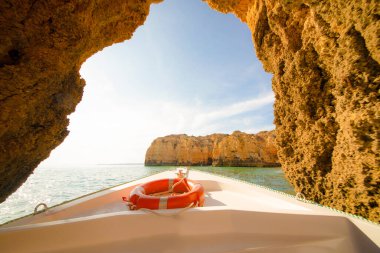 Güzel kayalıkların ve kemerlerin arka planında turuncu can simidi olan beyaz bir tekne.
