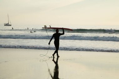Arrifana, Aljezur, Portekiz. 09 numara. 29 yaşında. 2020. Gün batımı plajında sörf tahtası taşıyan sörfçü. Sörfçü spor sağlığı ve seyahat konsepti.
