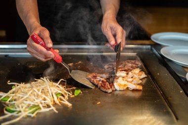 Şefin elleri teppanyaki yerine spatula ile. Sebze pişirmek et ve deniz ürünleri sıcak hibachi ızgara masasında. Geleneksel Japonca. Teppan gösterisi. Dünya mutfağı kavramı