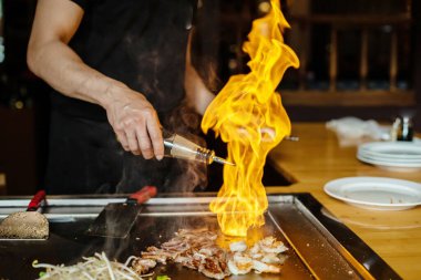 Şefin elleri teppanyaki yerine spatula ile. Sebze pişirmek et ve deniz ürünleri sıcak hibachi ızgara masasında. Geleneksel Japonca. Teppan gösterisi açık alevle