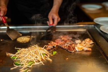 Şefin elleri teppanyaki yerine spatula ile. Sebze pişirmek et ve deniz ürünleri sıcak hibachi ızgara masasında. Geleneksel Japonca. Teppan gösterisi. Dünya mutfağı kavramı
