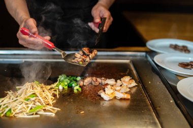 Şefin elleri teppanyaki yerine spatula ile. Sebze pişirmek et ve deniz ürünleri sıcak hibachi ızgara masasında. Geleneksel Japonca. Teppan gösterisi. Dünya mutfağı kavramı