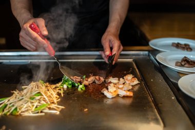 Şefin elleri teppanyaki yerine spatula ile. Sebze pişirmek et ve deniz ürünleri sıcak hibachi ızgara masasında. Geleneksel Japonca. Teppan gösterisi. Dünya mutfağı kavramı