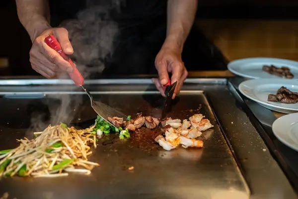 Şefin elleri teppanyaki yerine spatula ile. Sebze pişirmek et ve deniz ürünleri sıcak hibachi ızgara masasında. Geleneksel Japonca. Teppan gösterisi. Dünya mutfağı kavramı