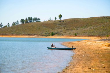 Madagaskar. 25 Ekim 2023 Tipik Madagaskar manzarası. Malagasy balıkçısı göl kıyısında bir teknede oturuyor.