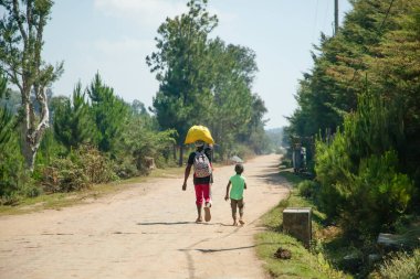 Madagaskar. 25 Ekim 2023 Tipik Madagaskar manzarası. Yol boyunca yürüyen parlak elbiseli insanlar. Kafalarında ağır yük taşıyan kadınlar, sepetler ve çantalar