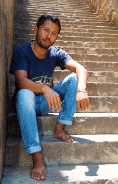 Yakın plan portre genç yakışıklı Malagasy adam gülümsüyor, merdivenlerde oturuyor, telefonla konuşuyor..