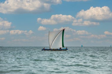 Morondava, Madagaskar. 18 Ekim 2023. Ev yapımı ahşap pirogue teknesindeki Malagasy balıkçısı ev yapımı basit yelkenli altında ağla balık yakalar. seçici odak