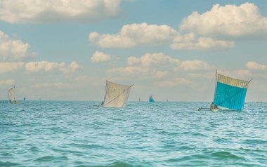 Morondava, Madagaskar. 18 Ekim 2023. Ev yapımı ahşap pirogue teknesindeki Malagasy balıkçısı ev yapımı basit yelkenli altında ağla balık yakalar. seçici odak