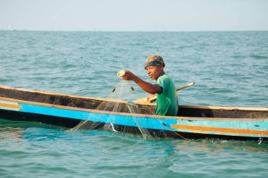 Morondava, Madagaskar. 18 Ekim 2023. Ev yapımı ahşap pirogue teknesindeki kötü niyetli balıkçı ağla balık yakalar. seçici odak, yakın plan