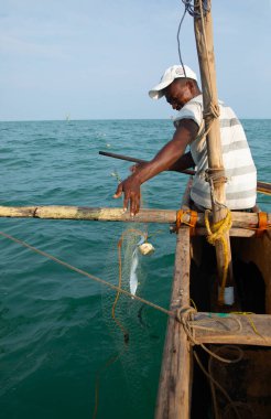 Morondava, Madagaskar. 18 Ekim 2023. Ev yapımı ahşap pirogue teknesindeki kötü niyetli balıkçı ağla balık yakalar. seçici odak, okyanusun yakın görüntüsü