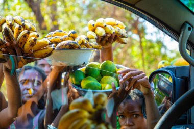 Antsirabe, Madagaskar 19 Ekim 2023. Morondava 'dan Antsirabe' ye giden yol Madagaskar 'ın merkezindeki köyden geçiyor. Yerel halk araba sürücülerine meyve satar. Kızlar araba camından meyve sepetleri tutarlar.