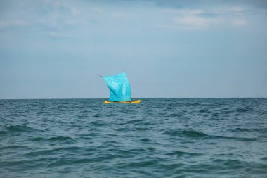 Morondava, Madagaskar. 18 Ekim 2023. Ev yapımı ahşap pirogue teknesindeki Malagasy balıkçısı ev yapımı basit yelkenli altında ağla balık yakalar. Seçici odaklanma. Okyanus manzarası