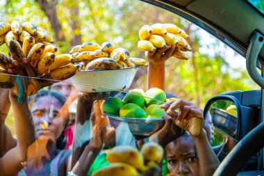 Antsirabe, Madagaskar 19 Ekim 2023. Morondava 'dan Antsirabe' ye giden yol Madagaskar 'ın merkezindeki köyden geçiyor. Yerel halk araba sürücülerine meyve satar. Kızlar araba camından meyve sepetleri tutarlar.