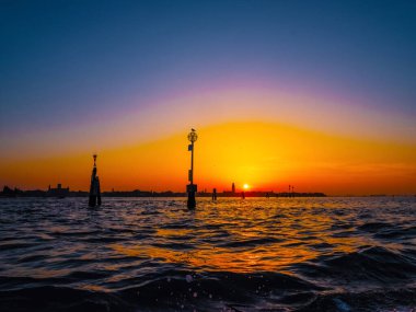 Venedik, İtalya. 29 Ekim 2022 Venedik silueti gün batımında batan güneşin parlak turuncu-kırmızı ışınlarında. Sudan manzara