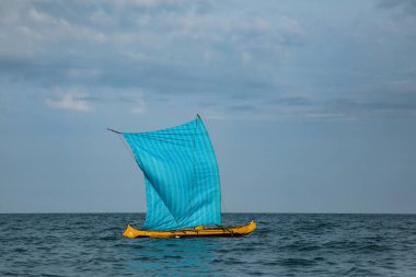 Morondava, Madagaskar. 18 Ekim 2023. Ev yapımı ahşap pirogue teknesindeki Malagasy balıkçısı ev yapımı basit yelkenli altında ağla balık yakalar. Seçici odaklanma. Okyanus manzarası