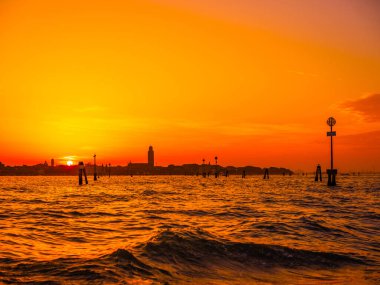 Venedik, İtalya. 29 Ekim 2022 Venedik silueti gün batımında batan güneşin parlak turuncu-kırmızı ışınlarında. Sudan manzara