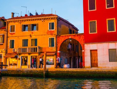 Venedik, İtalya. 29 Ekim 2022 Venedik silueti gün batımında batan güneşin parlak turuncu-kırmızı ışınlarında. Sudan manzara. Gün batımında kanalın kıyısında parlak renkli evler