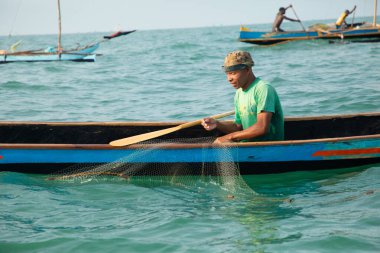 Morondava, Madagaskar. 18 Ekim 2023. Ev yapımı ahşap pirogue teknesindeki kötü niyetli balıkçı ağla balık yakalar. seçici odak, okyanusun yakın görüntüsü