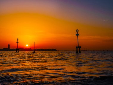 Venedik, İtalya. 29 Ekim 2022 Venedik silueti gün batımında batan güneşin parlak turuncu-kırmızı ışınlarında. Sudan manzara