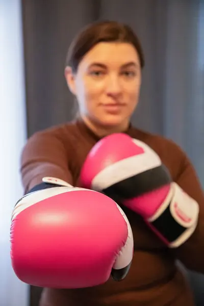 a young woman in boxing gloves on a gray background looks at the camera, stands in a boxing stance