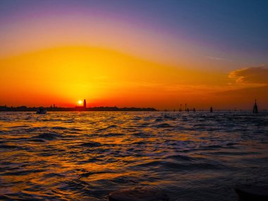 Venedik, İtalya. 29 Ekim 2022 Venedik silueti gün batımında batan güneşin parlak turuncu-kırmızı ışınlarında. Sudan manzara