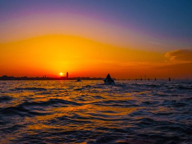 Venedik, İtalya. 29 Ekim 2022 Venedik silueti gün batımında batan güneşin parlak turuncu-kırmızı ışınlarında. Sudan manzara