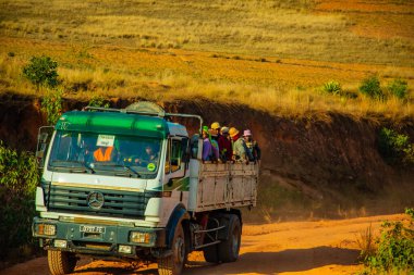 Madagaskar, 10 numara. 22 yaşında. 2023 Malagasy 'li bir grup, güneşli bir günde çamurlu, tozlu bir yolda dururken kamyonun arkasına biniyor.