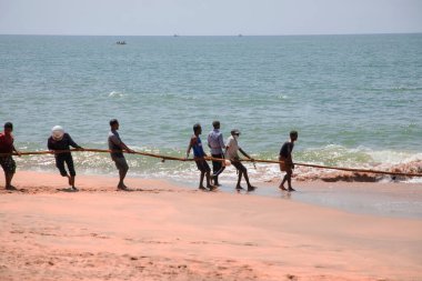 Unawatuna, Sri Lanka 09 Şubat 2023 'te farklı renklerde yaz kıyafetleri giyen bir grup adam balıkçıların Güney Sri Lanka sahilindeki büyük balık ağını çekmelerine yardım ediyor. Sıkı takım çalışması..