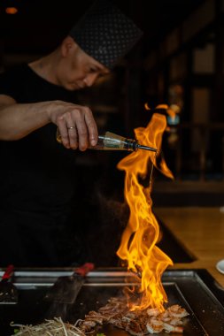Berlin, Almanya 08. 16 yaşında. 2023. Teppanyaki şefi bir Japon et lokantasında Teppan 'da yemek pişiriyor. Japon şef ateşli bir gösteri sergiliyor ve alev saçıyor
