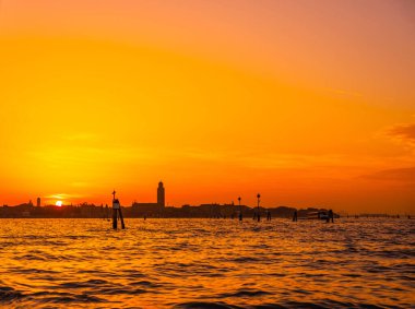 Venedik, İtalya. 29 Ekim 2022 Venedik silueti gün batımında batan güneşin parlak turuncu-kırmızı ışınlarında. Sudan manzara