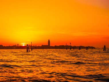 Venedik, İtalya. 29 Ekim 2022 Venedik silueti gün batımında batan güneşin parlak turuncu-kırmızı ışınlarında. Sudan manzara