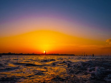 Venedik, İtalya. 29 Ekim 2022 Venedik silueti gün batımında batan güneşin parlak turuncu-kırmızı ışınlarında. Sudan manzara