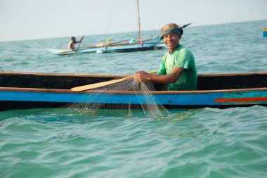 Morondava, Madagaskar. 18 Ekim 2023. Ev yapımı ahşap pirogue teknesindeki kötü niyetli balıkçı ağla balık yakalar. seçici odak, okyanusun yakın görüntüsü