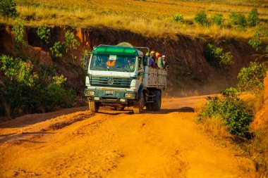 Madagaskar, 10 numara. 22 yaşında. 2023 Malagasy 'li bir grup, güneşli bir günde çamurlu, tozlu bir yolda dururken kamyonun arkasına biniyor.