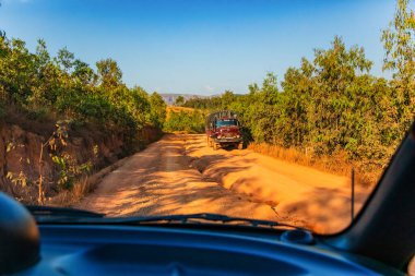 Madagaskar 22. - 10. 2023. Kırmızı toz ve çamur yolu büyük deliklerle kötü durumda. Madagaskar 'da yağmur mevsiminde rotalar son derece kötüdür. Büyük eski bir kamyon ters istikamette gidiyor.