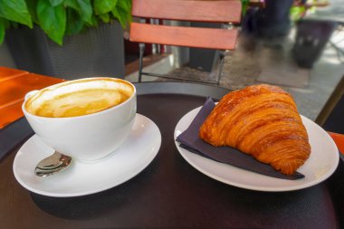 Kahvaltı manzarası, bir demet kruvasan ve kafenin arka planında bir fincan kahve.