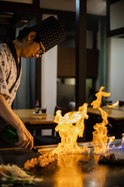 Berlin, Almanya 05. 09 numara. 2019. Teppanyaki şefi bir Japon et lokantasında Teppan 'da yemek pişiriyor. Japon şef ateşli bir gösteri sergiliyor ve alev saçıyor