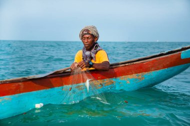 Morondava, Madagaskar. 18 Ekim 2023. Ev yapımı ahşap pirogue teknesindeki kötü niyetli balıkçı ağla balık yakalar. seçici odak, okyanusun yakın görüntüsü